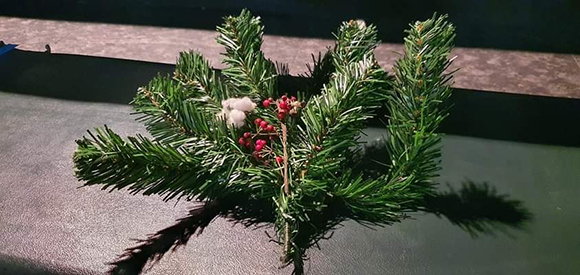 등받이가 없는 긴 객석 의자의 중앙에 거리두기를 표시하기 위한 크리스마스 장식이 놓여 있다. 녹색의 전나무 가지에 빨간 열매와 하얀 솜이 붙어 있다.