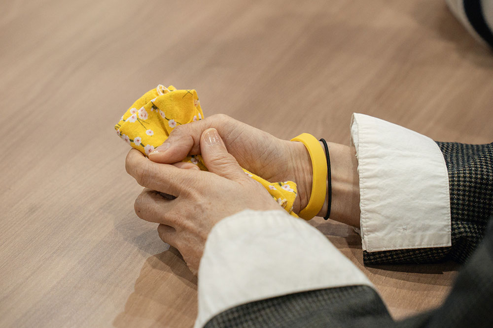 책상 위에 놓인 배우 김순덕의 손을 클로즈업한 사진. 꽃무늬가 들어간 노란 손수건을 곱게 접어 양손에 꼭 쥐고 있다. 오른쪽 손목에 노란 팔찌가 드러나 있다.