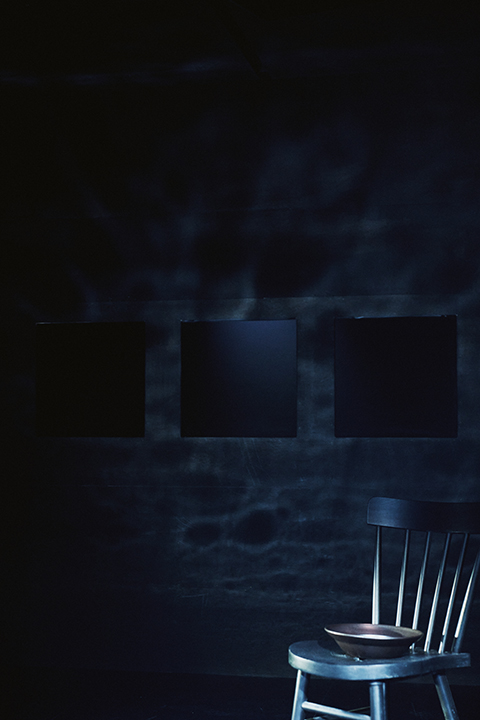 <이토록 가깝게>의 공간 사진. 전체적으로 짙은 푸른빛의 어두운 공간에 나무 의자가 하나 있다. 
            의자 위에는 검은색의 그릇이 놓여 있고, 공간의 뒷벽에는 세 개의 검은 스크린이 나란히 걸려 있다. 뒷벽과 천장에 일렁이는 물 그림자 같은 것이 비친다.