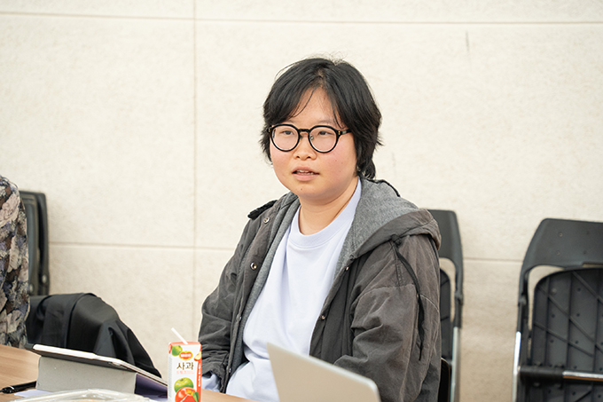 좌담 참여자 임대륜. 귀를 덮는 짧은 머리에 검은색의 동그란 뿔테 안경을 썼다.
연보라색의 라운드 티셔츠 위에 짙은 회색의 후드 재킷을 입었다.