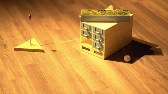 마룻바닥에 삼각형, 사각형 모양의 오브제가 있고, 실에 매달린 탁구공이 보인다.