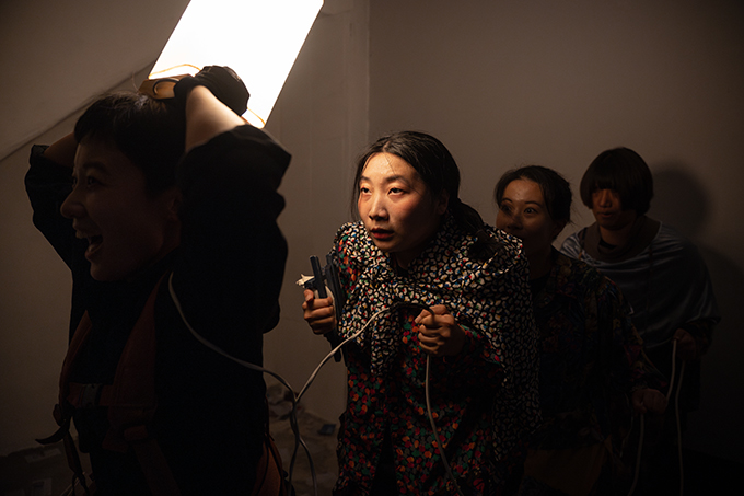 <쇼 팔다>의 공연 사진. 어두운 공간에 네 명의 인물이 일렬로 줄지어 서 있다. 제일 앞의 사람은 두 손으로 직육면체 모양의 조명을 들어 머리 위에 얹고 신나는 표정을 짓고 있다. 
            그의 뒤로 어깨를 잔뜩 웅크린 채 몽롱한 표정으로 정면을 응시하는 인물의 얼굴이 환하게 보인다. 
            뒤쪽으로 서 있는 두 사람에게는 조명이 잘 닿지 않는다. 이들은 모두 제일 앞선 사람이 들고 있는 조명에서 이어진 배선을 손에 붙잡고 있다.