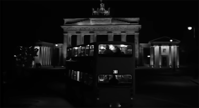 U2 – Stay(Faraway, So Close!) 뮤직비디오의 첫 장면을 캡처한 이미지. 
            독일 베를린 브란덴부르크 문 앞을 지나가는 2층 버스를 뒤에서 촬영했다. 
            흑백의 이미지이지만 거리와 버스의 불빛이 선명하고, 그 불빛에 버스의 1층과 2층 맨 뒤 좌석에 앉아 있는 사람들의 모습이 도드라진다.