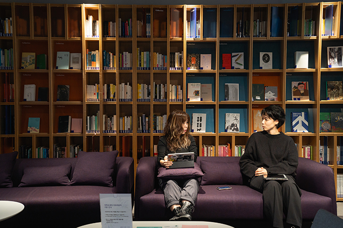 성수연과 강수연이 한 팔 정도의 간격을 두고 앉아 서로를 마주 보고 있다.
두 사람이 앉은 소파 옆으로 꼭 같은 소파가 나란히 놓여 있고, 뒤로는 여섯 단짜리 책장이 벽면을 가득 채우고 있다.