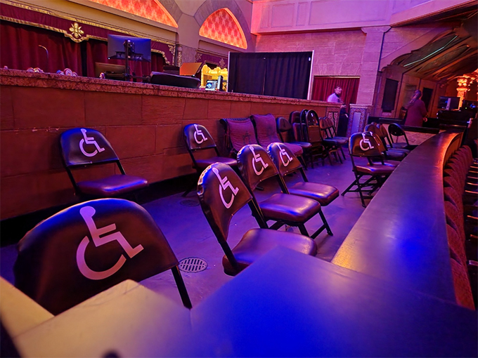 극장 좌석의 가장 마지막 줄, 넓은 공간에 접이식 의자 여러 개가 비치되어 있다. 
                등받이에 휠체어 이용인의 이미지가 그려져 있다.