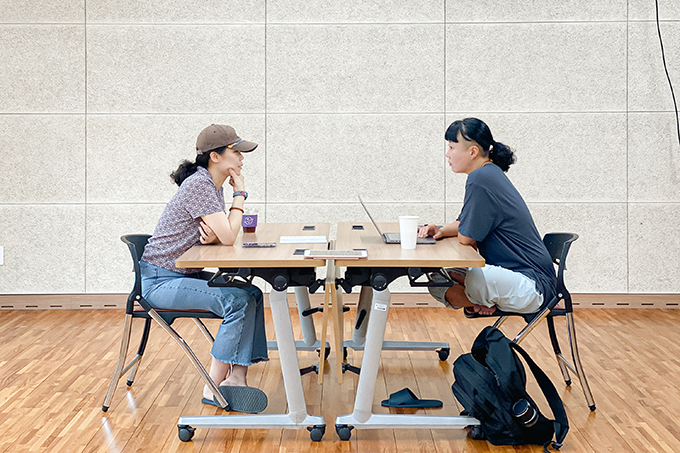 연출가 김미란과 연출가 김수정이 마주 보고 앉은 모습을 옆에서 찍은 사진이다. 
            둘 다 몸을 앞으로 기울여 서로에게 집중하고 있다.