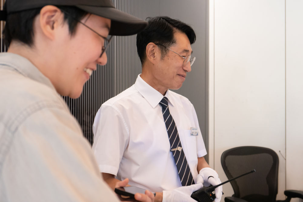 두산아트센터 인포메이션 데스크에 선 김정훈과 박세련이 같은 곳을 바라보며 웃고 있는 옆 모습을 촬영한 사진이다.