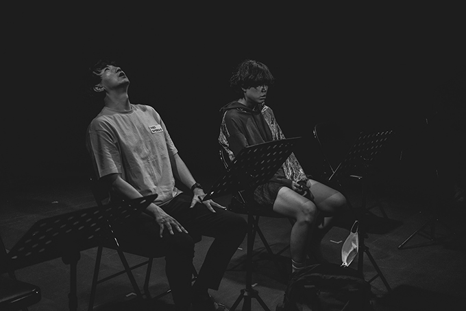 낭독공연 <레드 스피도>의 사진. 사진은 전체적으로 어두운 흑백으로 촬영되었다.
두 배우가 각자 보면대를 앞에 두고 앉아 있으며, 왼쪽으로 보면대가 하나 더 보인다.
왼쪽 배우는 왼쪽 가슴에 red speedo가 적힌 반소매 티와 긴 바지를 입고 허벅지에 양손을 올린 채 하늘을 바라본다.
오른쪽 배우는 두 눈을 덮는 앞머리에 굵은 웨이브의 단발머리를 하고 왼쪽 팔과 오른쪽 등 부분이 반짝이로 되어 있는 후드와 반바지를 입었다.
그의 앞에 놓인 보면대에 흰 마스크가 하나 걸렸다.