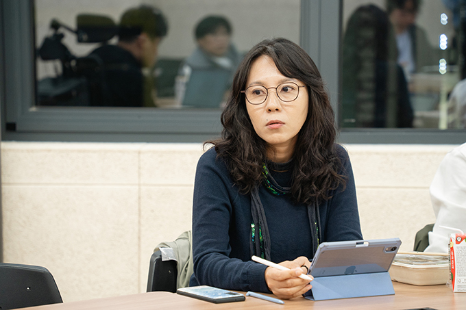 좌담 참여자 양근애. 어깨 밑으로 내려오는 웨이브가 들어간 머리에, 검은 테의 안경을 쓰고 있다.
남색 니트를 입었고, 초록색 계열의 스팽글이 박힌 검은색 머플러를 느슨하게 두르고 있다.