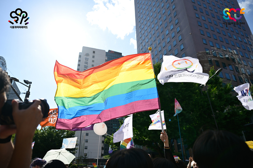 서울퀴어퍼레이드2024의 현장 사진. 행렬 사이에서 휘날리는 무지개 깃발을 화면 가득 촬영하였다.