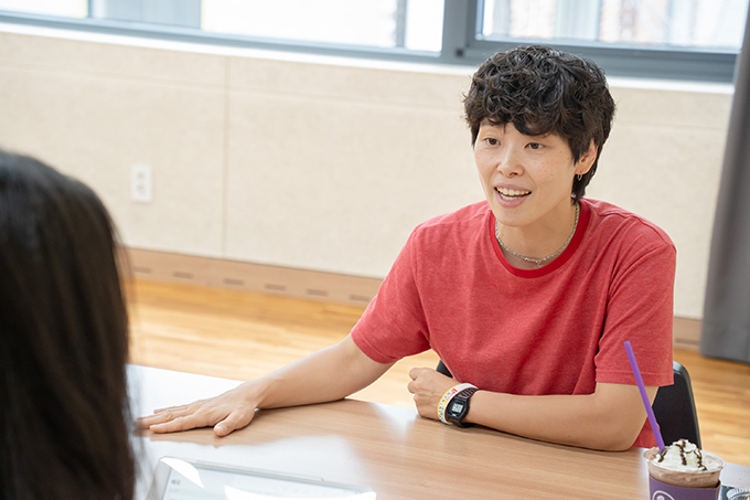 배우 권은혜가 오른손을 곧게 펴서 책상을 짚은 채 웃는 얼굴로 이야기하고 있다.