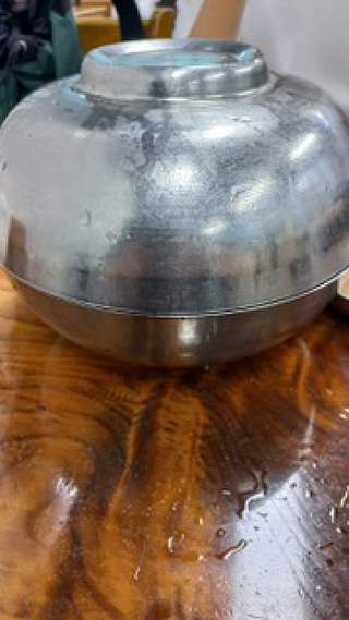 스테인리스 냉면 그릇 하나가 놓여 있고, 그 위에 똑같은 냉면 그릇을 뒤집어 얹어두었다. 그릇이 빛을 받아 희미하게 주변을 반사한다.