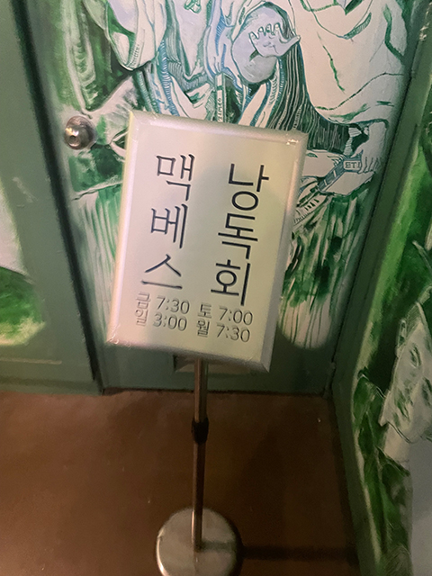 독립서점 풀무질로 입장하는 계단 참에 ‘맥베스 낭독회’가 적힌 안내판이 놓여있다.
흰 종이에 검은 글씨가 적혀있으며 ‘맥베스’는 바탕체로, ‘낭독회’는 돋움체로 세로 쓰기 되어있고, 하단에는 요일별 공연시간이 돋움체 가로쓰기로 적혀있다.
계단 참에는 초록색으로 그림이 가득 그려져 있는데, 오른쪽 벽면에 윤동주 시인의 졸업사진을 그린 것이 보인다.