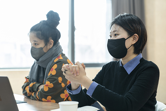 편집위원 김연재. 짧은 커트 머리에 검은색 니트를 입고, 안에 푸른색 셔츠를 받쳐 입었다. 두 손을 앞으로 모아 맞잡고 이야기하고 있다.
