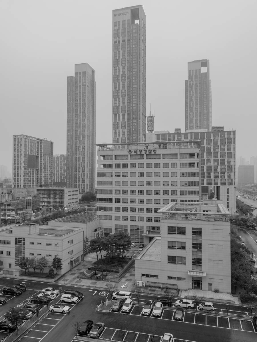 흑백으로 해양경찰청의 전경을 찍은 사진. 해양경찰청 뒤로 높게 솟은 고층 건물이 보인다. 가장 높은 건물에는 ‘1st WORLD’라고 쓰여 있다.