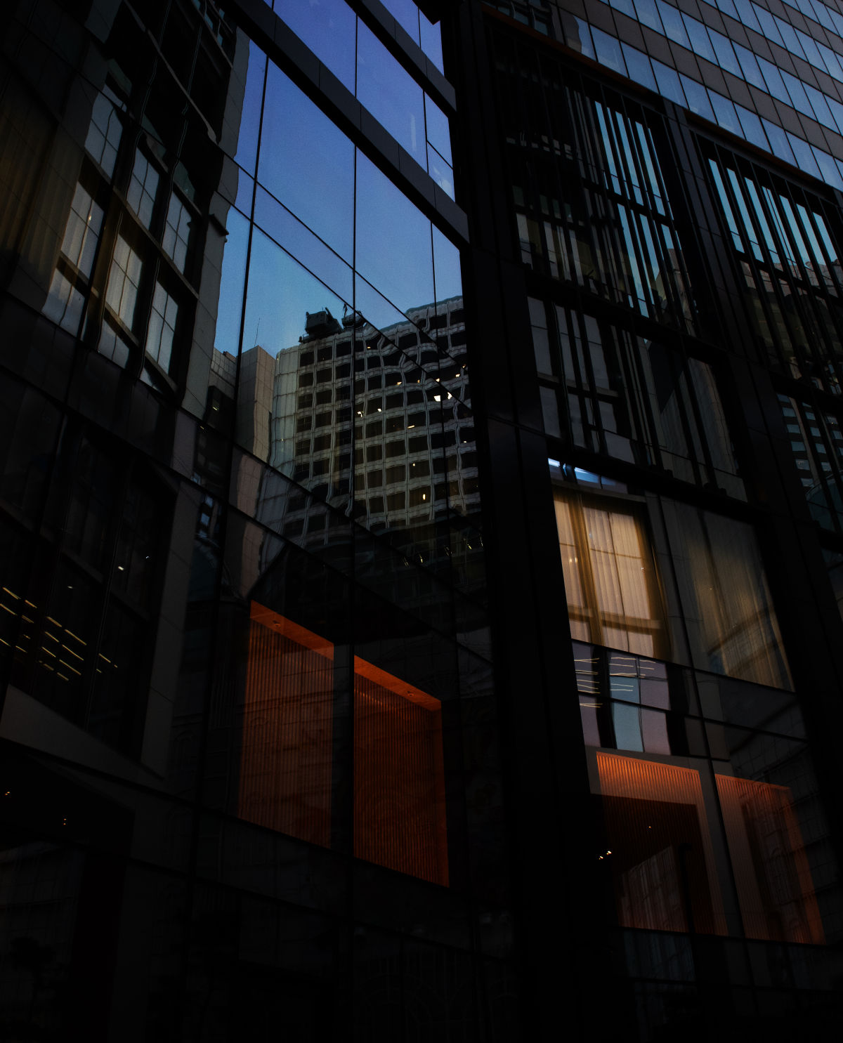 한 건물의 외부를 찍은 사진. 사진 중간 부분의 외창에는 맞은 편 건물이 반사되어 비치고, 좌측 상단, 우측 하단에는 이 건물의 내부에서 나오는 빛들이 새어나온다.