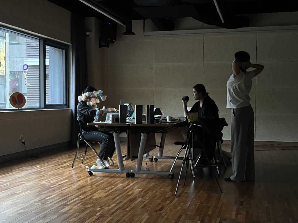 서울문화재단 서울연극센터 다목적실에서 유다영, 임미정, 니키노가 릴레이 글쓰기 퍼포먼스를 하고 있다. 이날 세 사람은 한 책상에서 2시간씩 돌아가며 글을 썼고, 나머지 시간에 다른 구성원은 곁에서 자유롭게 머무르는 시간을 보냈다. 이나래 작가는 프랑스에 있어 화상회의를 통해 참여하였다. 이 화면은 전체 과정을 기록한 결과물 〈내가 살아있었을 때〉의 스틸샷으로, 니키노는 글을 쓰고 있고, 유다영은 니키노를 촬영하고 임미정은 스트레칭을 하고 있다.