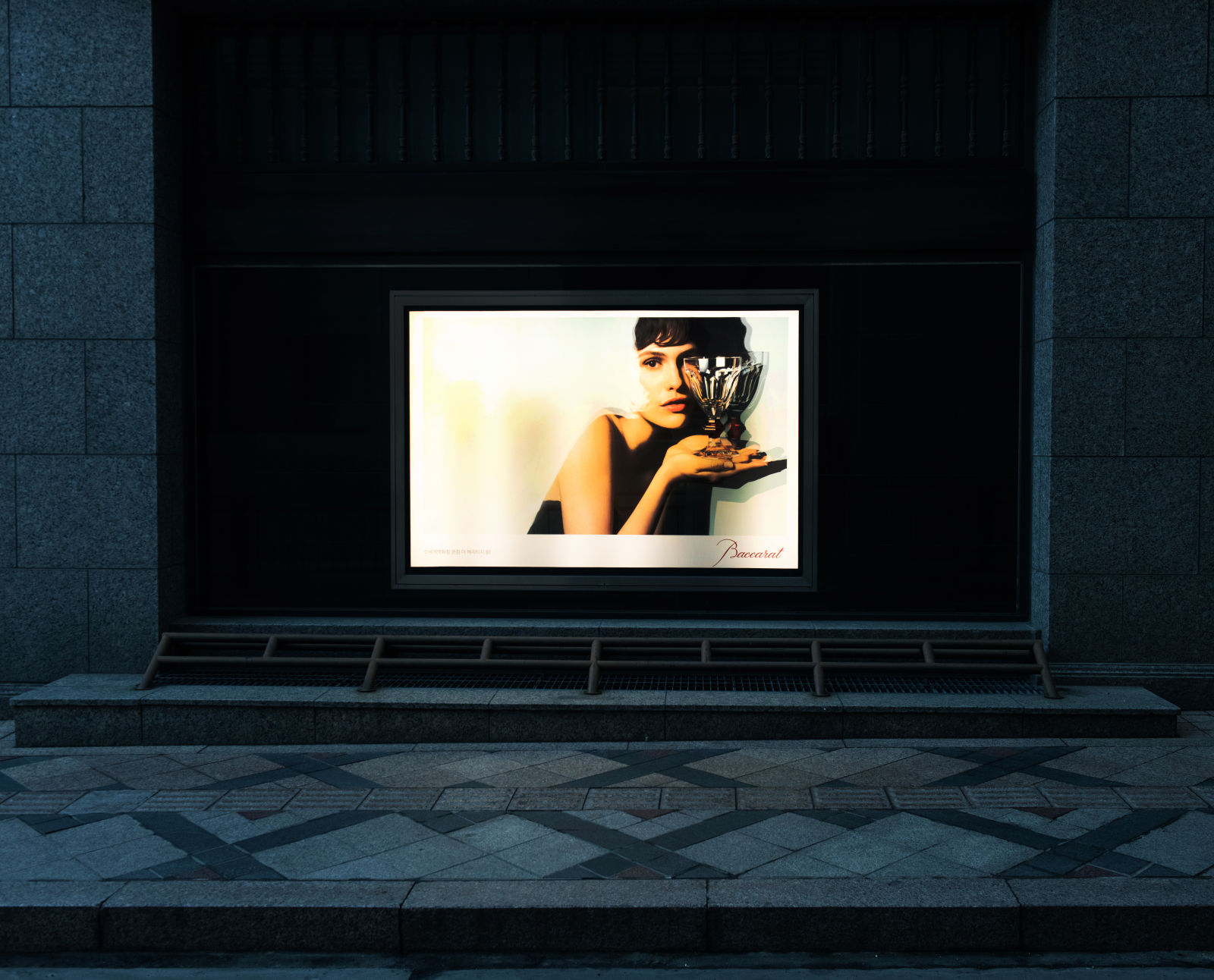어두운 공간 속, 정중앙에 광고판 이미지만이 빛나고 있다. 검은 옷을 입은 인물이 반짝이는 잔을 들고 카메라를 응시하고 있다.